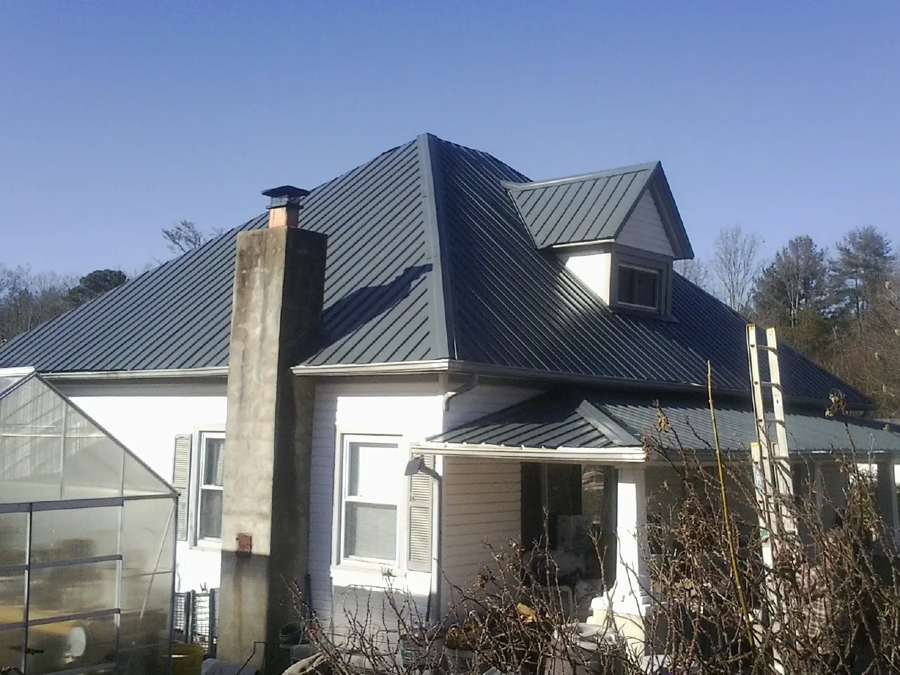 Dark blue standing seam metal roof on a white farmhouse with dormer — Slate & Tile Roof Repair by Roofing Brothers in Schererville