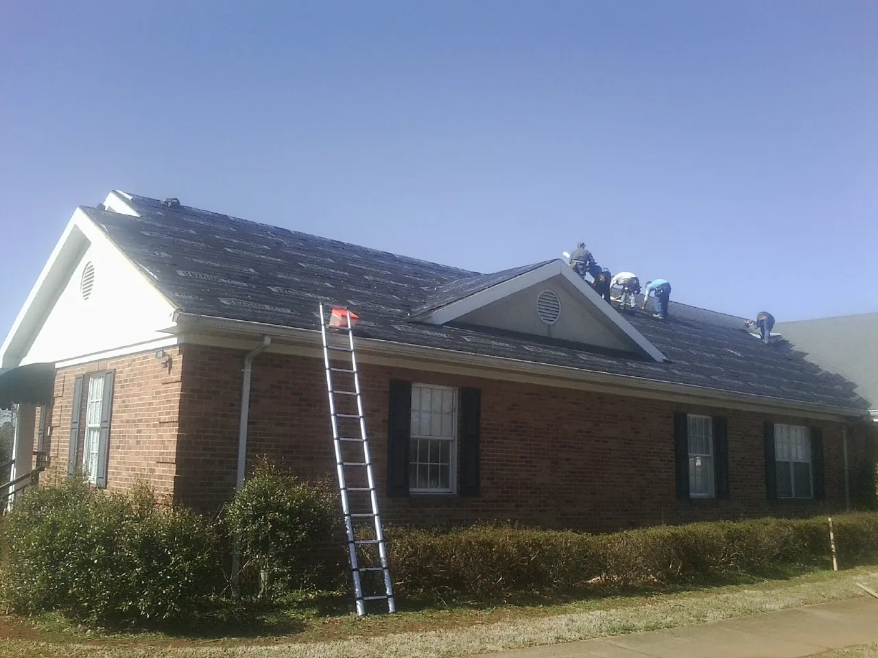 Crew tearing shingles off a brick ranch roof with a ladder set — Emergency Roof Repair work by our crew in Schererville