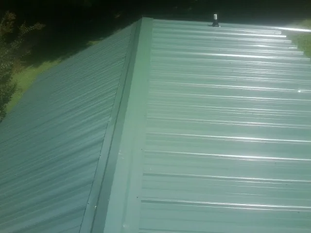 New green metal panels meeting at the ridge of a roof — Flat Roof Repair work by our crew in Schererville