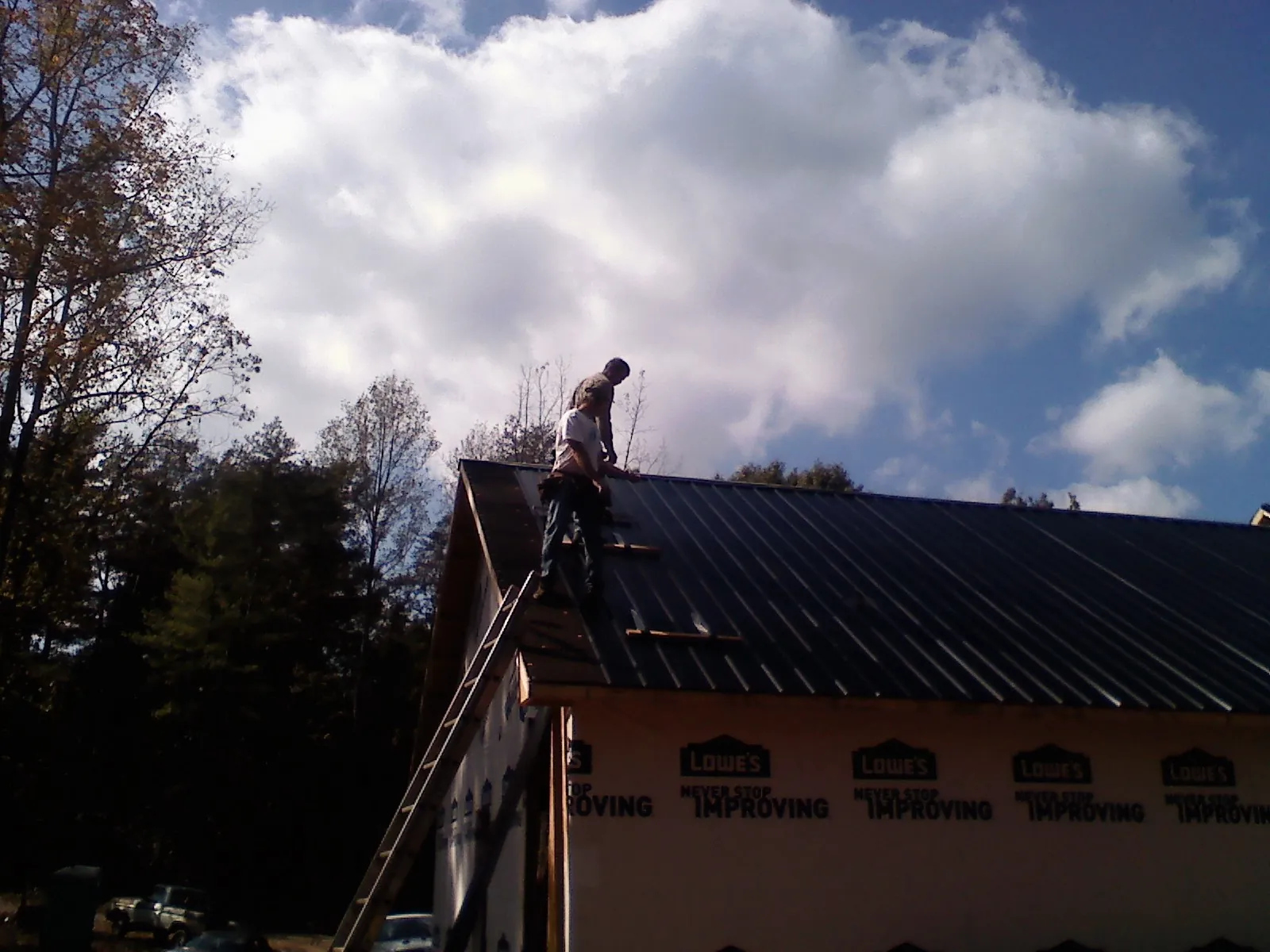 Roofer fastening dark metal panels high against a cloudy sky, from a Roof Inspection job in Schererville