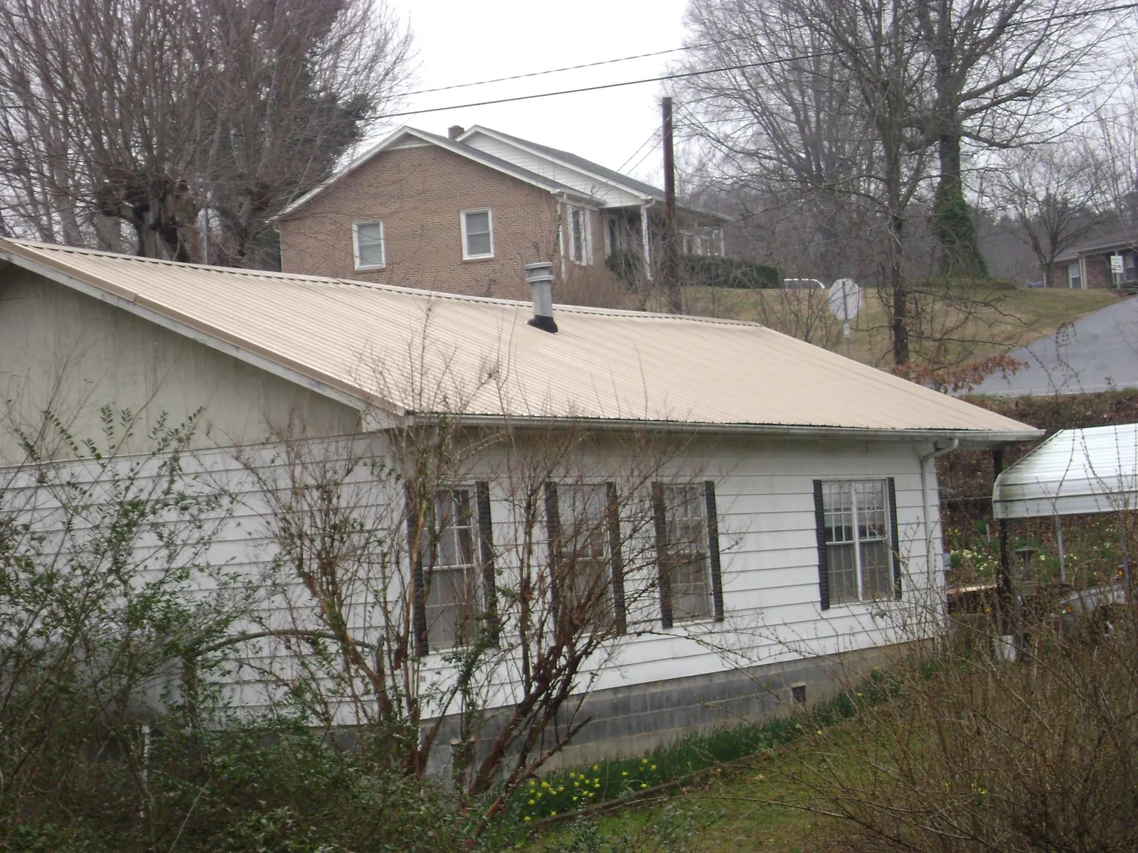 Tan metal roof on a white sided house set into a hillside — Commercial Roofing by Roofing Brothers in Schererville